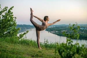 Ein junger Turner macht Yoga in der Natur in einem Park gegen den Himmel und verwendet eine Kombination aus traditionellen Yoga-Posen, Pilates und sanftem Tanz. Verbindung mit der Natur. foto