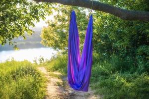 Eine lila Hängematte für Aerial Yoga hängt im Sommer bei Sonnenuntergang an einem Baum in der Natur. foto