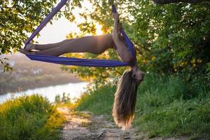 Eine junge Turnerin macht Aerial Yoga in der Natur des Parks mit einer Kombination aus traditionellen Yoga-Posen, Pilates und sanftem Tanz foto