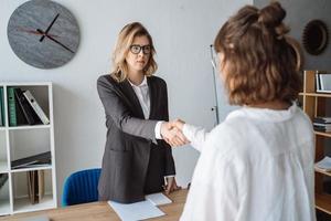 Zwei Geschäftsfrauen geben sich im Büro die Hand foto