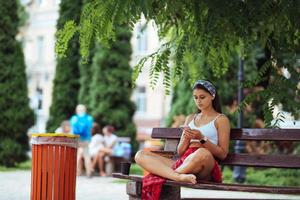 Frau, die ein Smartphone im Park benutzt und auf einer Bank sitzt foto