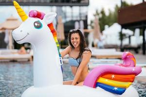 Frau auf aufblasbarer Einhorn-Spielzeugmatratze schwimmt im Pool. foto