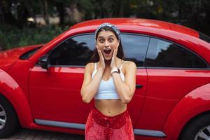 Porträt einer hübschen kaukasischen Frau, die gegen ein neues rotes Auto steht foto