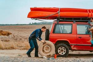 mann rollt ein neues ersatzrad zu einem 4x4-geländewagen foto