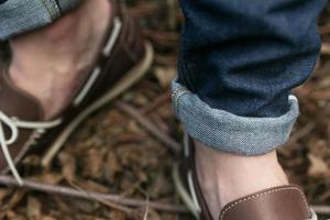 Füße des Mannes in den authentischen Stiefeln und Selvedge-Jeans, auf dem Hintergrund von Zweigen foto