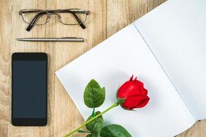 rote rosen auf leerem notizbuchtagebuch mit smartphone-valentinsgrußkonzept foto
