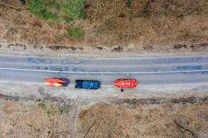 Mehrere Autos mit Kajaks auf dem Dachträger fahren auf der Straße zwischen Bäumen foto