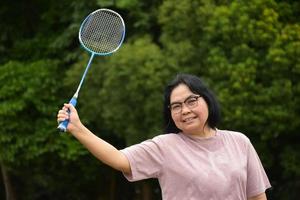 Outdoor-Badmintonspiel, weicher und selektiver Fokus auf weißem Federball, verschwommenem asiatischem Frauen- und Baumhintergrund, Konzept für Outdoor-Badmintonspiel in Freizeit und täglichen Aktivitäten. foto