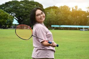 Outdoor-Badmintonspiel, weicher und selektiver Fokus auf weißem Federball, verschwommenem asiatischem Frauen- und Baumhintergrund, Konzept für Outdoor-Badmintonspiel in Freizeit und täglichen Aktivitäten. foto