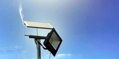 Mini-Solar- oder Photovoltaikzellen-Panel, installiert auf Metallmast mit Flutlicht-LED, verschwommener, bewölkter und blauer Hintergrund, Konzept zur Nutzung natürlicher Energie aus der Sonne im täglichen Leben des Menschen. foto