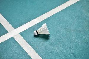 Cremeweißer Badmintonfederball auf grünem Boden im Indoor-Badmintonplatz, verschwommener Badmintonhintergrund, Kopierraum foto