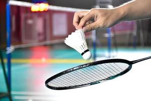 Badmintonschläger und alter weißer Federball, der den Spieler in den Händen hält, während er ihn über das Netz vor ihm serviert, verwischen den Hintergrund des Badmintonplatzes und selektiven Fokus foto