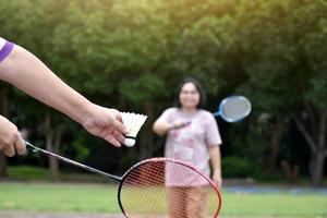 Outdoor-Badmintonspiel, weicher und selektiver Fokus auf weißem Federball, verschwommenem asiatischem Frauen- und Baumhintergrund, Konzept für Outdoor-Badmintonspiel in Freizeit und täglichen Aktivitäten. foto