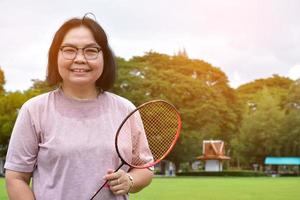 Outdoor-Badmintonspiel, weicher und selektiver Fokus auf weißem Federball, verschwommenem asiatischem Frauen- und Baumhintergrund, Konzept für Outdoor-Badmintonspiel in Freizeit und täglichen Aktivitäten. foto