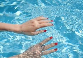 Nahaufnahme von Frauenhänden mit Maniküre in Rot unter klarem Poolwasserhintergrund, Mode- und Sportkonzept foto