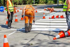 Ein Team von Straßenarbeitern markiert mit weißer Farbe einen Fußgängerüberweg auf der Fahrbahn. foto