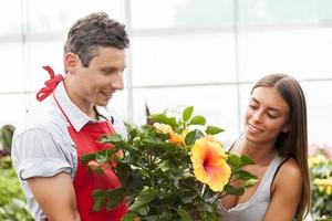 Ein lächelnder Verkäufer verkauft eine Pflanze an einen hübschen Kunden foto