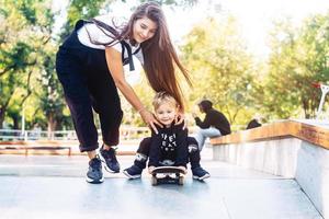 Die junge Mutter bringt ihrem kleinen Jungen das Skateboardfahren bei foto