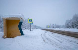 Landstraße mit Anschlussstelle, Autospuren in einer Schmutzschnee-Nahaufnahme. Waldweg an einem bewölkten Wintertag. Blick von einer Bushaltestelle. Transport, gefährliches Fahren, Winterreifen, abgelegene Orte. foto