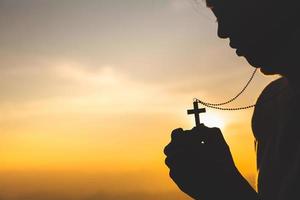 Silhouette einer christlichen jungen Frau, die bei Sonnenaufgang mit einem Kreuz betet, Hintergrund des christlichen Religionskonzepts. foto