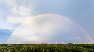 Regenbogen im blauen bewölkten Himmel über Wald und Stadt foto