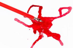 Draufsicht auf rote Federspitze über rotem Tintenklecks auf Weiß foto