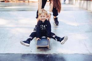 Die junge Mutter bringt ihrem kleinen Jungen das Skateboardfahren bei foto