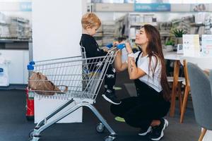 schöne mutter trägt ihren kleinen sohn im einkaufswagen foto