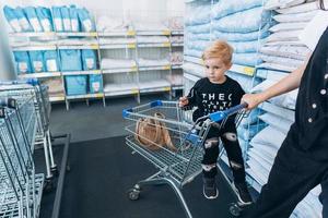 schöne mutter trägt ihren kleinen sohn im einkaufswagen foto