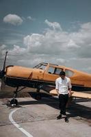 ein Mann, der auf dem Hintergrund eines kleinen einmotorigen Flugzeugs steht. foto