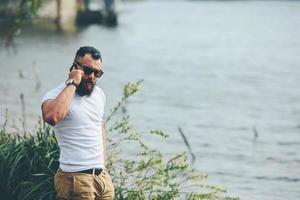 amerikanischer bärtiger Mann, der Telefon nahe dem Fluss benutzt foto