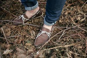 Füße des Mannes in den authentischen Stiefeln und Selvedge-Jeans, auf dem Hintergrund von Zweigen foto