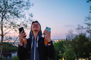 Der junge Mann im Park macht ein Foto auf zwei Smartphones