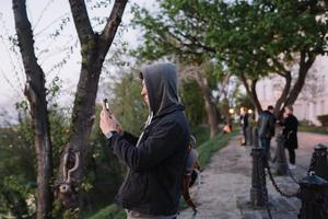 Der junge Mann im Park macht ein Foto auf zwei Smartphones