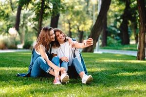 Zwei Freundinnen, die im Park sitzen, ruhen sich aus und machen ein Selfie foto