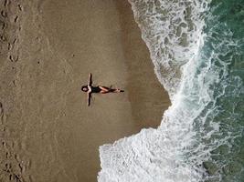 Luftdraufsicht junge Frau, die auf dem Sandstrand und den Wellen liegt foto