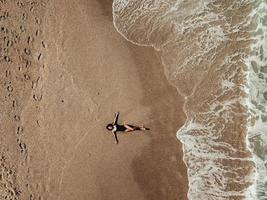 Luftdraufsicht junge Frau, die auf dem Sandstrand und den Wellen liegt foto