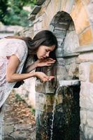 Schönes, junges Mädchen trinkt Quellwasser im Freien foto