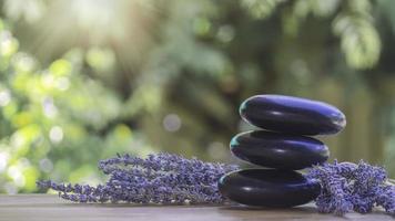 Gleichgewichts- und Wellness- oder Gesundheitskonzept mit einem Haufen schwarzer Spa-Steine auf Holz und Spikes aus blühendem Lavendel mit Aromatherapie. Seitenansicht und Landschaftskomposition fühlen sich entspannt an. foto