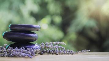 Gleichgewichts- und Wellness- oder Gesundheitskonzept mit einem Haufen schwarzer Spa-Steine auf Holz und Spikes aus blühendem Lavendel mit Aromatherapie. Seitenansicht und Landschaftskomposition fühlen sich entspannt an. foto