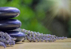 Gleichgewichts- und Wellness- oder Gesundheitskonzept mit einem Haufen schwarzer Spa-Steine auf Holz und Spikes aus blühendem Lavendel mit Aromatherapie. Seitenansicht und Landschaftskomposition fühlen sich entspannt an. foto