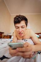 Nahaufnahme eines Mannes, der im Bett liegt und ein Smartphone im Innenbereich verwendet. foto