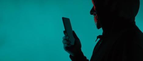 Anonymer Hacker und Gesichtsmaske mit Smartphone in der Hand. foto