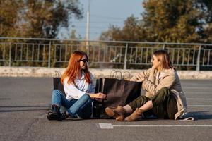 junge frauen mit einkaufstüten sitzen auf dem parkplatz foto