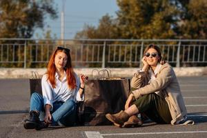 junge frauen mit einkaufstüten sitzen auf dem parkplatz foto