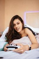 lustiges mädchen, das im bett liegt und videospiel spielt, controller hält foto