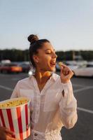 Junge süße Frau, die Popcorn auf einem Parkplatz eines Einkaufszentrums hält foto