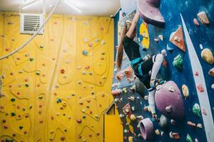 junge Frau, die eine hohe, künstliche Kletterwand im Innenbereich erklimmt foto