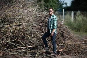 der Mann in den authentischen Stiefeln und Selvedge-Jeans auf dem Hintergrund von Ästen foto