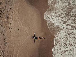 Luftdraufsicht junge Frau, die auf dem Sandstrand und den Wellen liegt foto